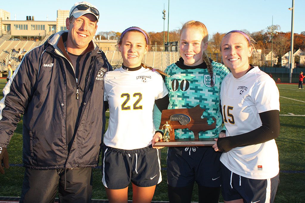GIRLS’ SOCCER head coach Mark Vermont celebrates winning the Pioneers’ third Division 3 North championship with senior captains, from left, Emily Scollard, Hannah Travers and Paige MacEachern after the Pioneers defeated archrival North Reading 3-1 at Manning Field on Saturday, Nov. 15. (Dan Tomasello Photo)