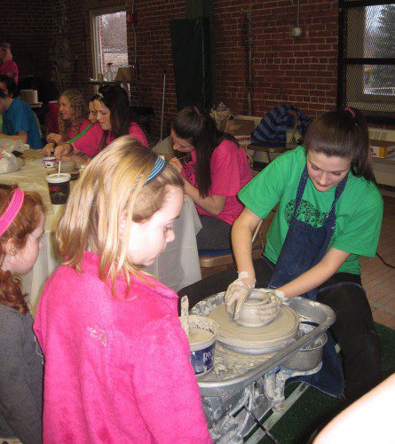 FALLON BRIGHT, a junior at Wakefield Memorial High School, showed a young girl how to make a vase using a pottery wheel during Visual Arts Night at the Americal Civic Center last night. The event drew hundreds of proud parents and art lovers. (Gail Lowe Photo)